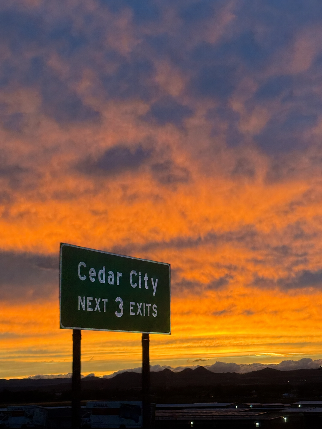 Cedar City highway sign beneath a vivid sunset over the mountains